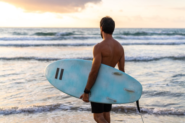 Junger kaukasischer Mann steht früh auf, um bei Sonnenaufgang zu surfen