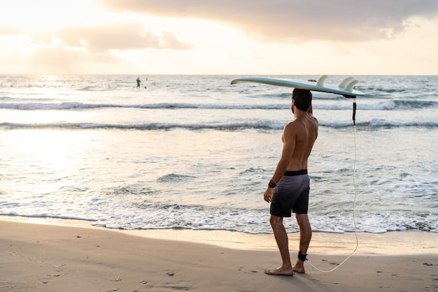Junger kaukasischer Mann steht früh auf, um bei Sonnenaufgang zu surfen