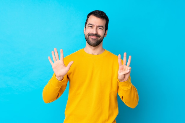 Junger kaukasischer Mann über der lokalisierten blauen Wand, die acht mit den Fingern zählt