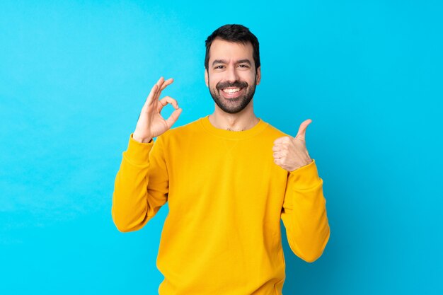 Junger kaukasischer Mann über isolierter blauer Wand, die ok Zeichen und Daumen hoch Geste zeigt