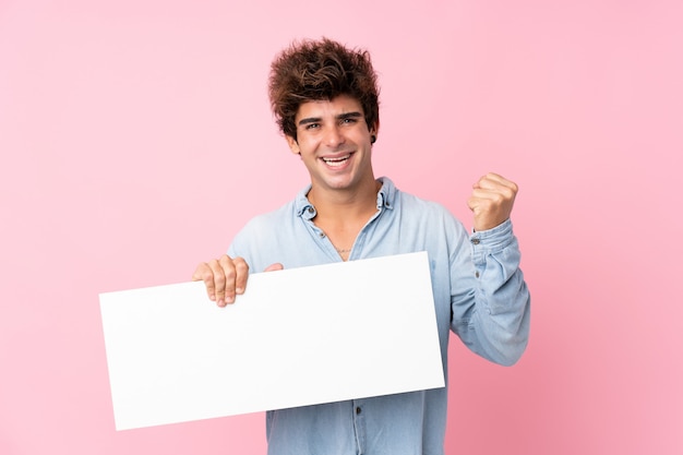 Junger kaukasischer Mann über isolierter rosa Wand, die ein leeres weißes Plakat für das Einfügen eines Konzepts hält