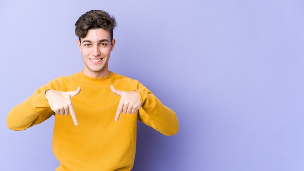 Junger kaukasischer Mann zeigt mit den Fingern nach unten, positives Gefühl.