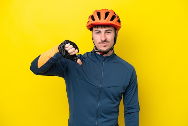 Junger kaukasischer Radfahrermann lokalisiert auf gelbem Hintergrund, der Daumen nach unten mit negativem Ausdruck zeigt