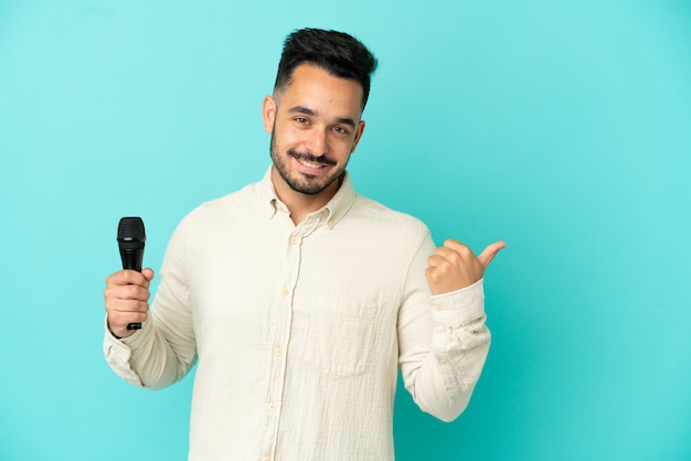 Junger kaukasischer Sänger Mann isoliert auf blauem Hintergrund, der auf die Seite zeigt, um ein Produkt zu präsentieren
