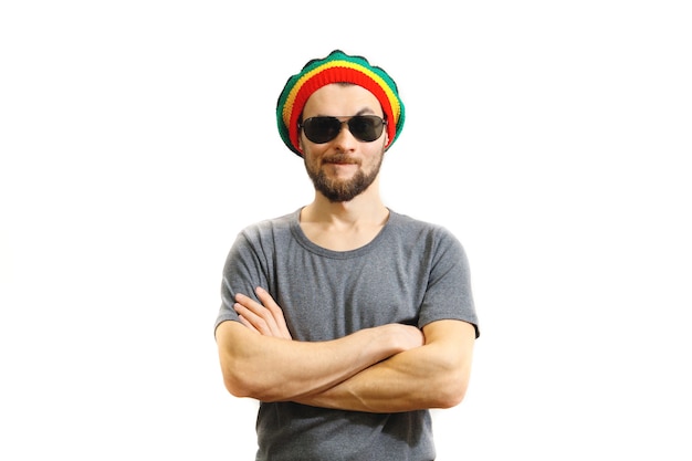 Junger kaukasischer Skeptiker mit Rasta-Hut, Sonnenbrille und grauem T-Shirt auf weißem Hintergrund.