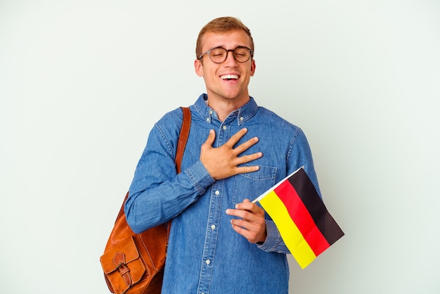 Junger kaukasischer Student, der Deutsch studiert, isoliert auf weißem Hintergrund, lacht laut und hält die Hand auf der Brust.