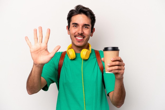 Junger kaukasischer Studentenmann, der Kaffee trinkt, isoliert auf weißem Hintergrund, lächelt fröhlich und zeigt Nummer fünf mit den Fingern.