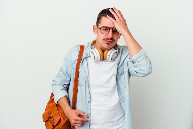 Junger kaukasischer Studentenmann, der Musik hört, die auf weißer Wand isoliert müde und sehr schläfrig ist, die Hand auf Kopf hält.