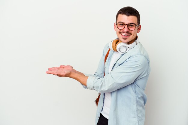 Junger kaukasischer Studentenmann, der Musik lokalisiert auf weißer Wand hört, die einen Kopienraum auf einer Handfläche hält.