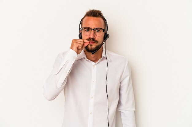 Junger kaukasischer Telemarketer-Mann mit Tätowierungen auf weißem Hintergrund mit Fingern auf den Lippen, die ein Geheimnis halten.