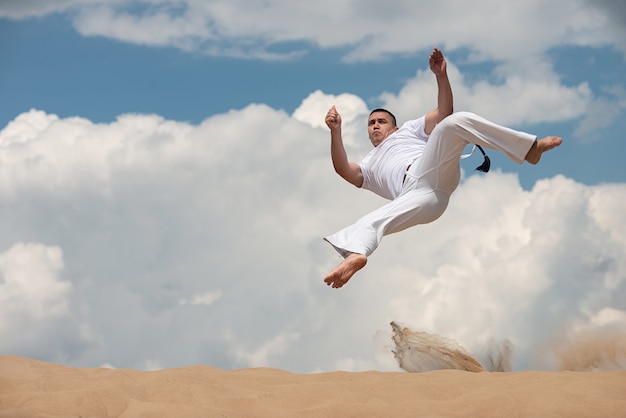 Junger Kerl bildet capoeira auf Himmel backround aus. Ein Mann führt den Tritt im Sprung martialisch aus