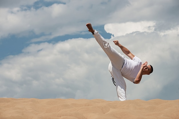 Junger Kerl bildet capoeira auf Himmel backround aus. Ein Mann führt den Tritt martialisch aus