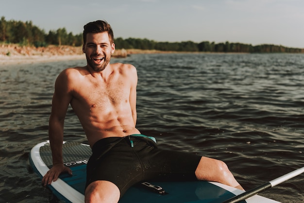 Foto junger kerl im badeanzug, der auf brandung im wasser ruht.