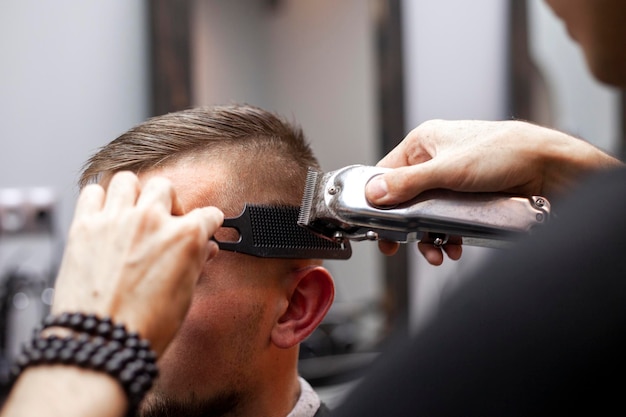 Junger Kerl macht einen kurzen Haarschnitt in einem Friseursalon mit einem Trimmer in der Nähe