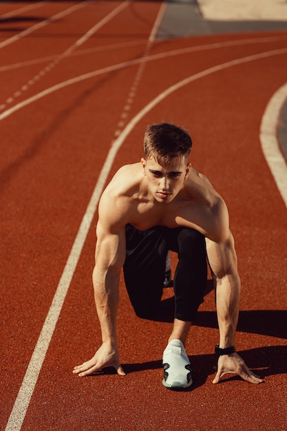 Junger Kerl mit athletischem Körper macht sich bereit zu laufen