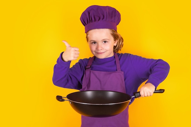 Junger Koch mit Kochpfanne. Kinderkoch. Kind in Kochuniform und Kochmütze, das im Studio Porträt von Speisen zubereitet