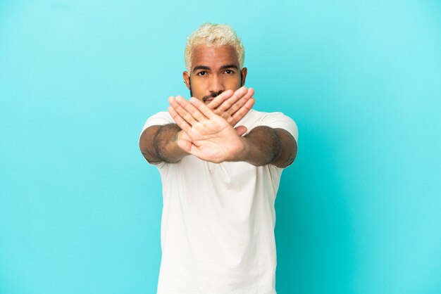 Junger kolumbianischer gutaussehender Mann isoliert auf blauem Hintergrund, der mit der Hand eine Stopp-Geste macht, um eine Handlung zu stoppen
