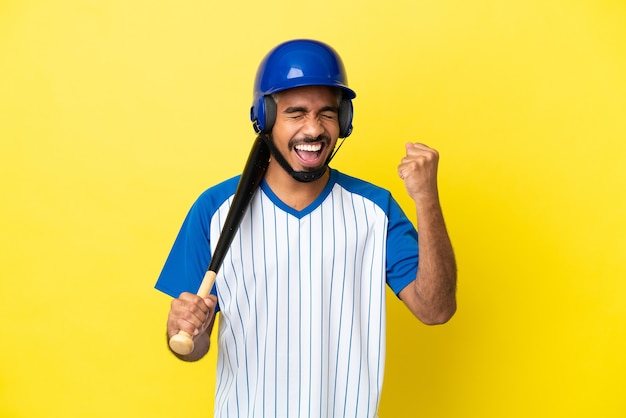 Junger kolumbianischer lateinischer Mann, der Baseball spielt, isoliert auf gelbem Hintergrund, der einen Sieg feiert