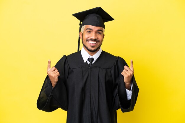 Junger kolumbianischer Mann mit Universitätsabschluss isoliert auf gelbem Hintergrund und zeigt eine großartige Idee