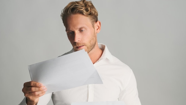 Foto junger konzentrierter blonder bärtiger geschäftsmann im hemd, das mit geschäftsdokumenten arbeitet, die auf weißem hintergrund lokalisiert werden