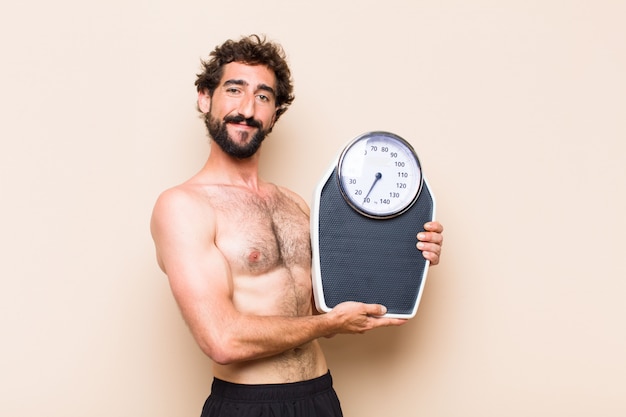 Junger kühler bärtiger Mann, der ein Gleichgewicht oder Skalenfitnesskonzept hält