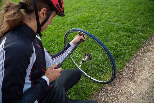 Junger kühler männlicher Radfahrer in der Sportkleidung und in Schutzhelm, die Luftkammer des Fahrrades reparieren, drehen herein Park