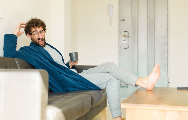 Junger kühler Mann, der auf einem Sofa am Wohnzimmer sitzt und fernsieht