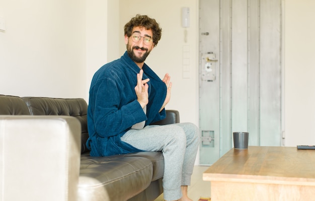 Junger kühler Mann, der auf einem Sofa am Wohnzimmer sitzt und fernsieht