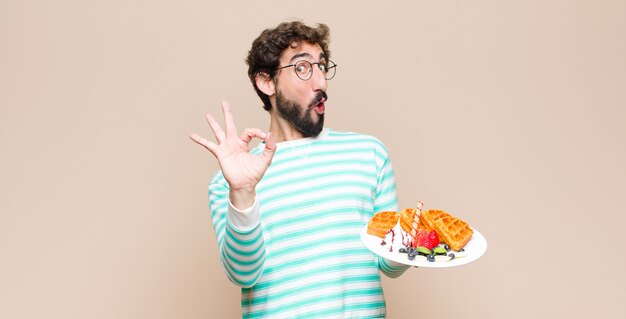 Junger kühler Mann mit Waffeln gegen flache Wand.