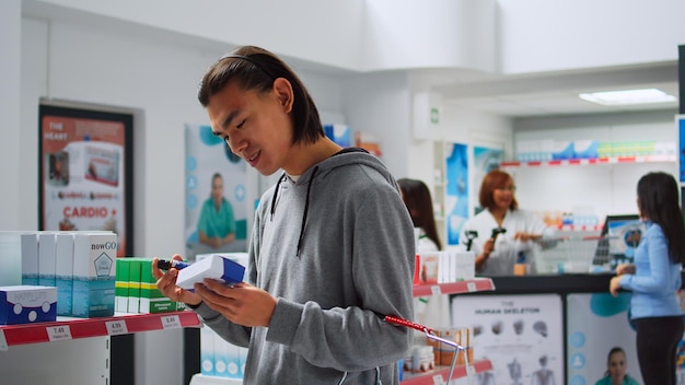 Junger Kunde überprüft Flaschen und Schachteln mit Medikamenten in der Apotheke und schaut sich die Gesundheitsmedikamente in den Regalen an. Untersuchung von Arzneimitteln und Vitaminen in Verpackungen, Apothekengeschäft.