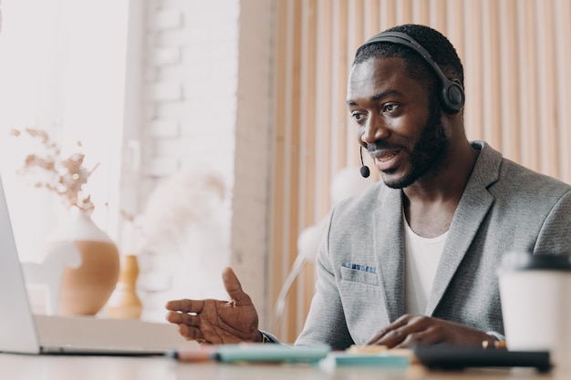 Junger lächelnder afrikanisch-amerikanischer Mann im Headset berät Kunden per Videoanruf auf dem Laptop