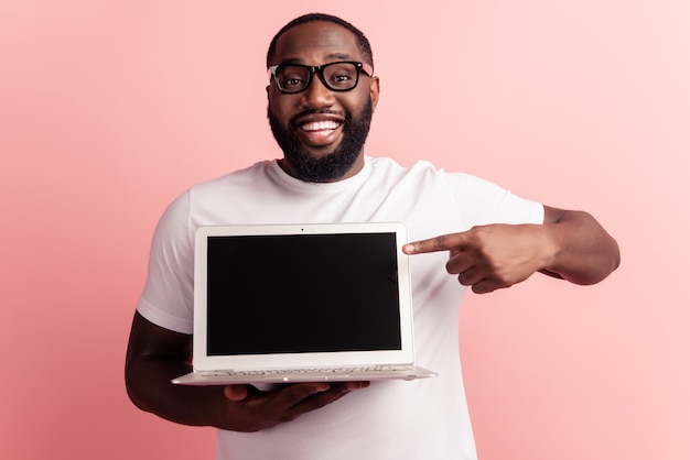Junger lächelnder afrikanischer Mann, der den leeren Raum des Laptops direkt mit dem Finger steht und verwendet
