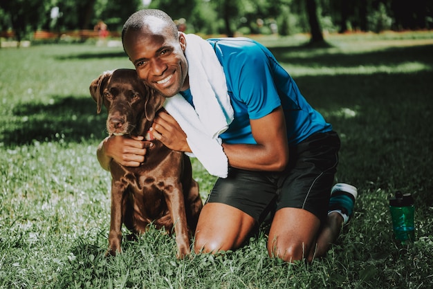 Junger lächelnder afrikanischer Mann, der Hund umarmt