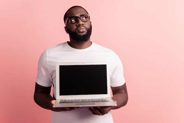 Junger lächelnder afrikanischer Mann, der steht und Laptop-Computer verwendet, zeigen Touchscreen-Look leeren Raum