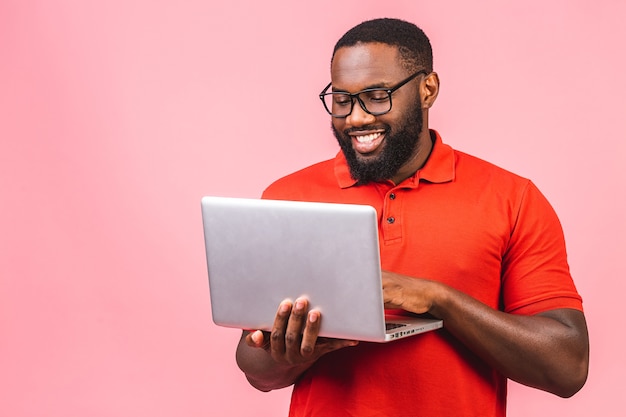 Junger lächelnder Afroamerikanermann, der steht und Laptop-Computer verwendet