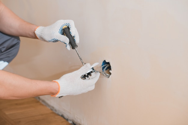 Junger lächelnder Elektriker, der elektrische Steckdose an der Wand im Haus installiert