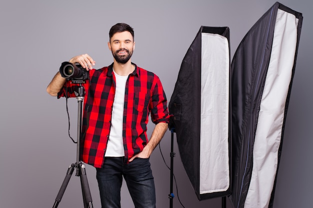 Junger lächelnder Fotograf mit Kamera im professionell ausgestatteten Studio.