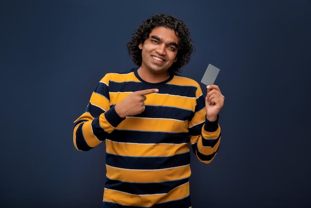 Junger lächelnder gutaussehender Mann, der mit einer Kredit- oder Debitkarte auf grauem Hintergrund posiert