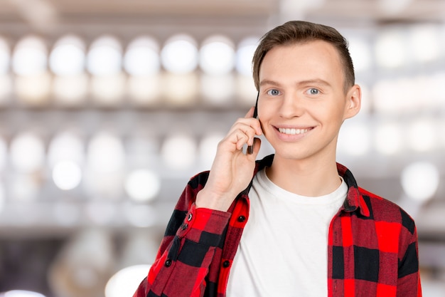 Junger lächelnder Mann, der auf dem Handy spricht