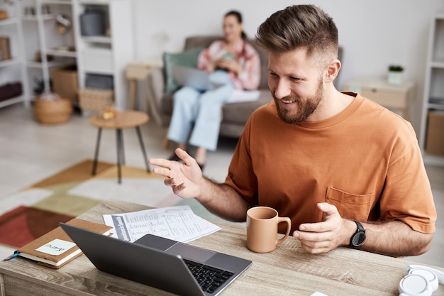 Junger lächelnder Mann in Freizeitkleidung, der während des Online-Unterrichts vor dem Laptop sitzt