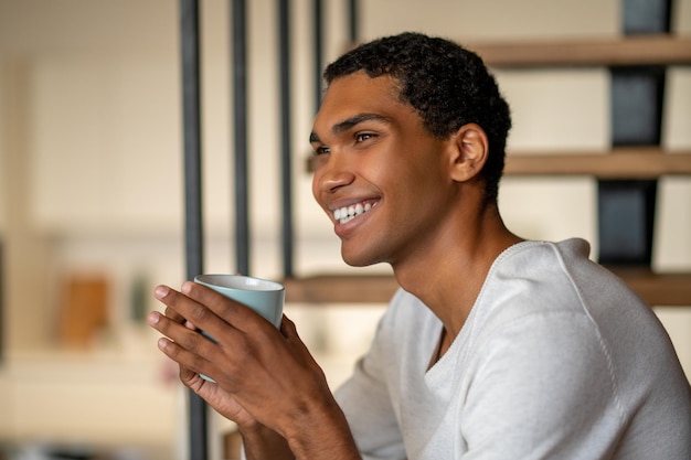 Junger lächelnder Mann zu Hause, der Kaffee trinkt und zufrieden aussieht