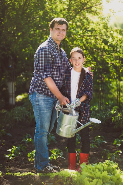 Foto junger lächelnder vater, der garten mit kleiner tochter bewässert