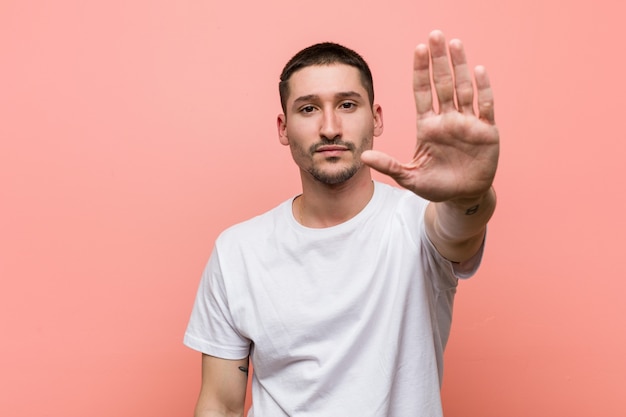 Junger lässiger Mann, der mit ausgestreckter Hand steht und Stoppschild zeigt, das Sie verhindert