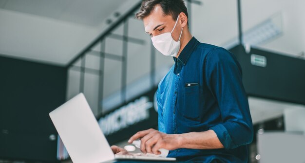 Junger lässiger Mann in der Schutzmaske, die seinen Laptop desinfiziert