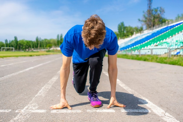 Junger Läufer Athlet in der niedrigen Startposition auf der Sportbahn im Stadion im Freien