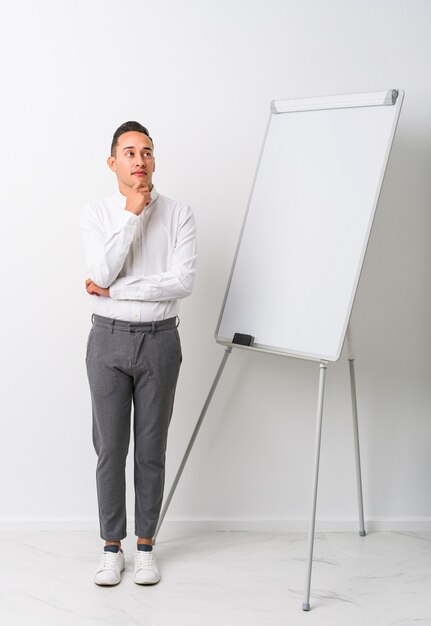 Junger lateinamerikanischer Coaching-Mann mit einem isolierten Whiteboard, das seitwärts mit zweifelhaftem und skeptischem Ausdruck schaut.