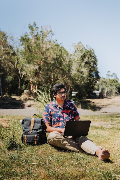 Junger lateinamerikanischer Mann der Vorderansicht, der vom See aus Remote-Online-Arbeit erledigt. Telearbeitskonzept Digitaler Nomade