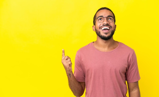 Junger lateinamerikanischer Mann isoliert auf gelbem Hintergrund nach oben zeigend und überrascht