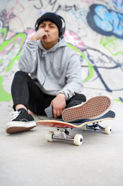 Junger lateinamerikanischer Skatermann, der mit Skateboard am Skatepark aufwirft.