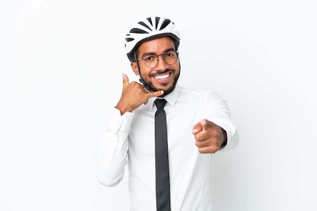 Junger lateinischer Geschäftsmann, der einen Fahrradhelm hält, der auf weißem Hintergrund isoliert ist und eine Telefongeste macht und nach vorne zeigt